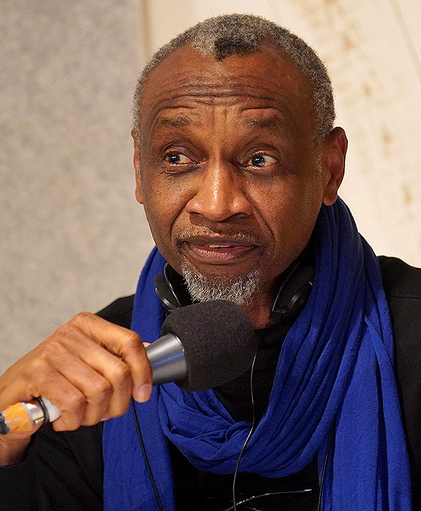 Dani Kouyaté speaking into a microphone, blue scarf, photographed by Alexander Gonschior in 2025